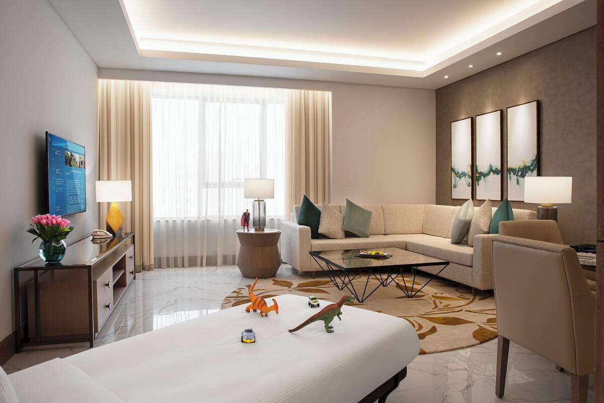 A modern hotel room with a large bed, a sofa, a coffee table, and a TV on a stand.