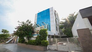 Un edificio moderno con fachada azul, entrada protegida por un portón y vegetación circundante.