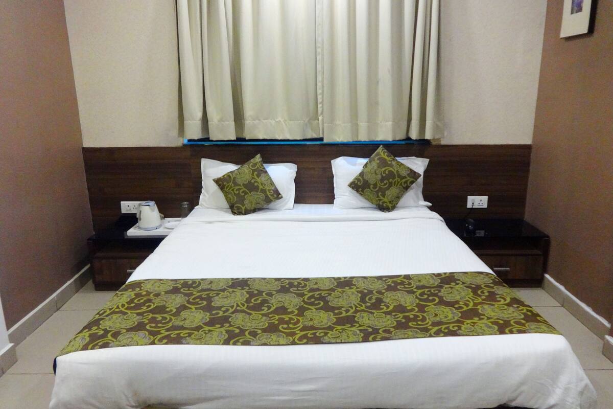 A hotel room with a bed, two pillows, a bedside table with a phone, and a window with curtains.