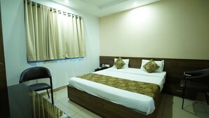 Habitación de hotel con una cama grande, dos sillas, un escritorio y un ventanal con cortinas.