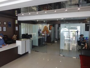 A reception area with a glass partition, a reception desk, and a statue. - Hotel Flora Inn (Nagpur)