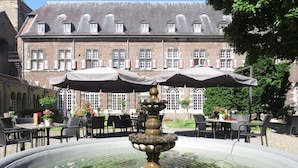 A courtyard with a fountain, outdoor seating, and a historic building in the background. - Abdij Rolduc (Kerkrade)