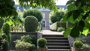 A formal garden leading to a classical building with a symmetrical design, featuring a central staircase, manicured hedges, and a brick wall. - Abdij Rolduc (Kerkrade)