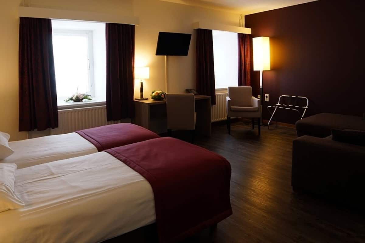 A hotel room with two beds, a desk, a chair, a sofa, and a TV.