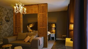 A bedroom with a sofa, a bed, a nightstand, a lamp, and a wooden partition. - Abdij Rolduc (Kerkrade)