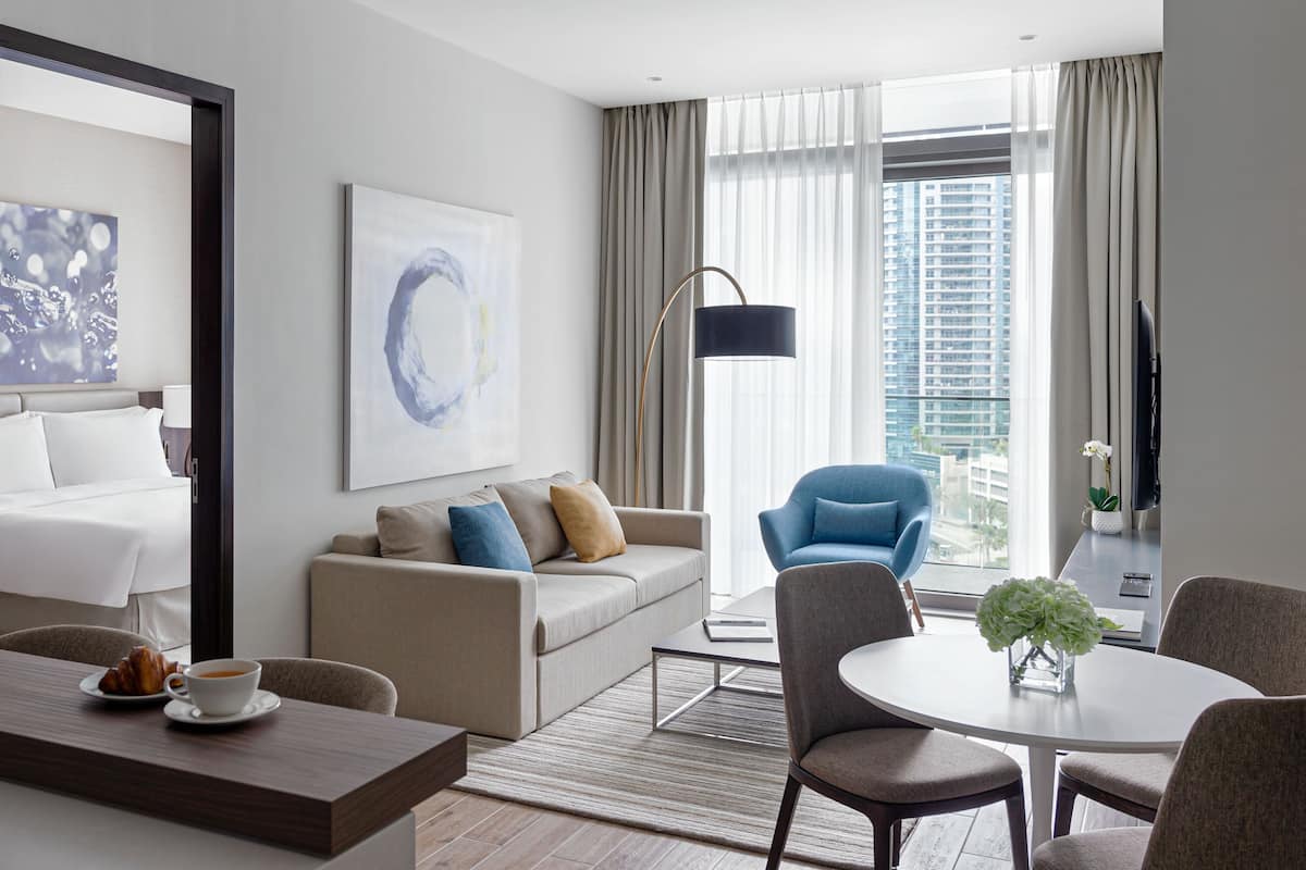 Een moderne hotelkamer met een bed, een bank, een eettafel en stadszicht door grote ramen.