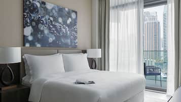 Une chambre d’hôtel moderne dotée d’un grand lit, de deux lampes de chevet, d’un balcon offrant une vue sur la ville et d’une peinture abstraite contemporaine accrochée au mur.