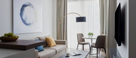 A modern hotel room with a sofa, coffee table, and a TV.