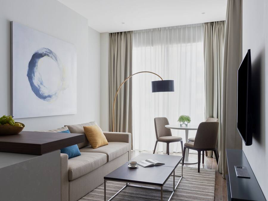 A modern hotel room with a sofa, coffee table, and a TV.