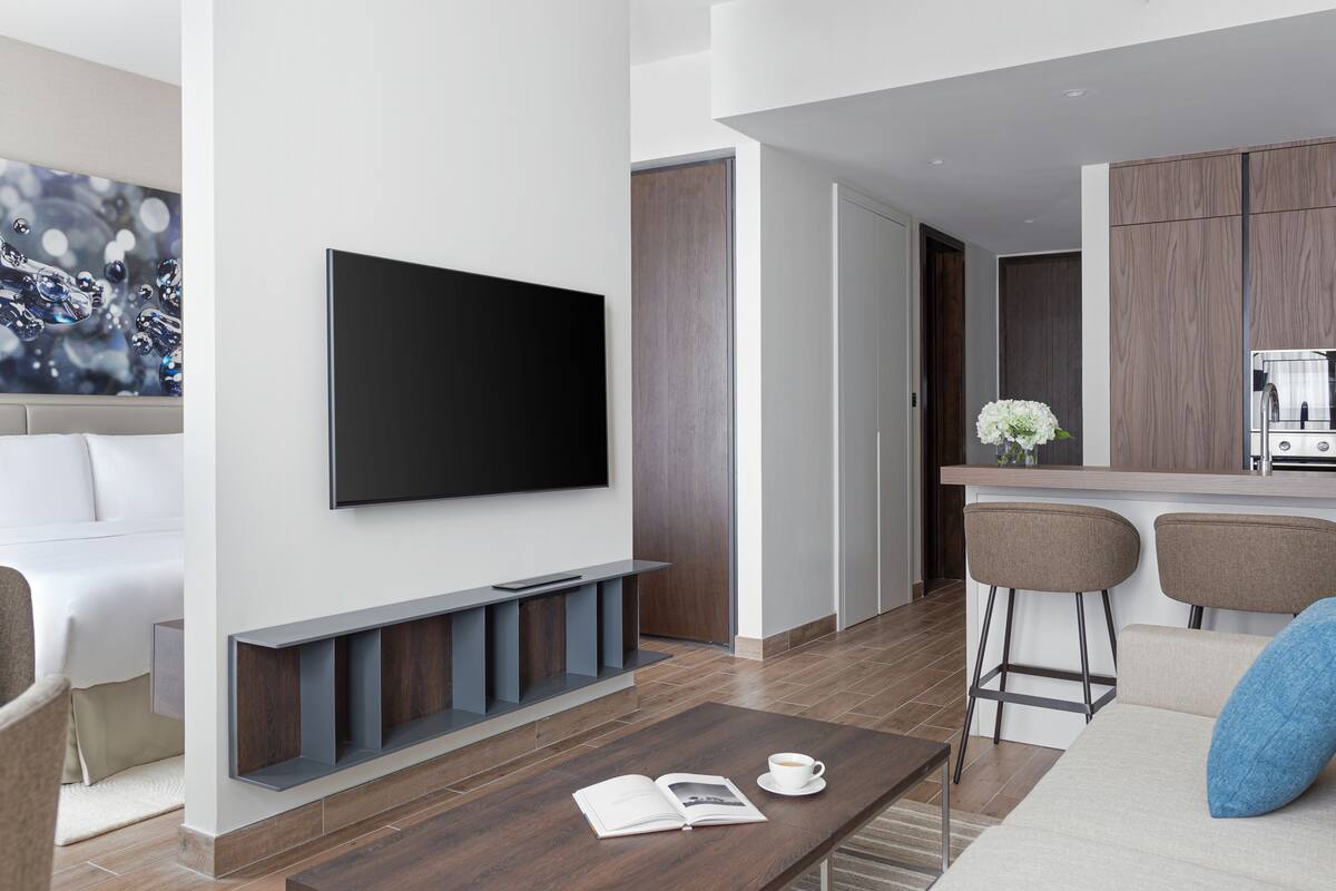 Een moderne woonkamer met een flatscreen televisie aan de muur, een salontafel met een boek en een kopje, en een bank met een blauw kussen.