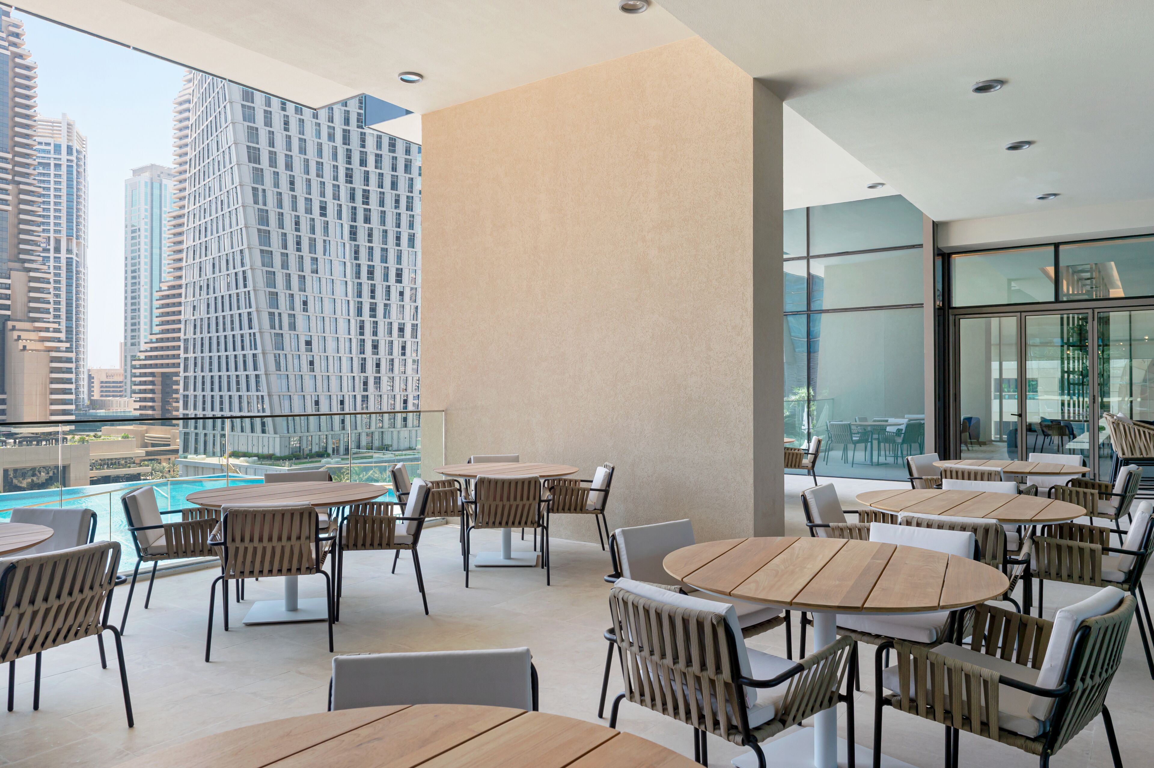 A rooftop terrace with round tables and chairs, overlooking a cityscape with modern buildings.