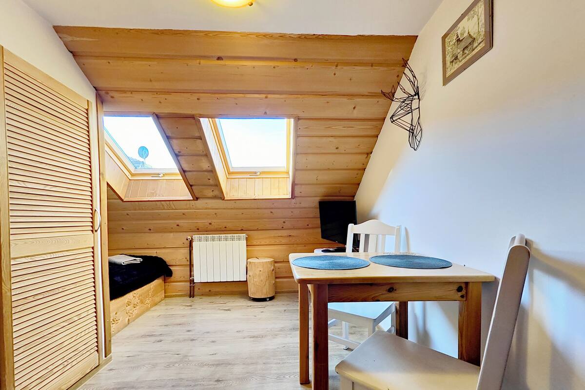 A cozy attic room with wooden beams, a skylight, a radiator, and a table with two chairs.