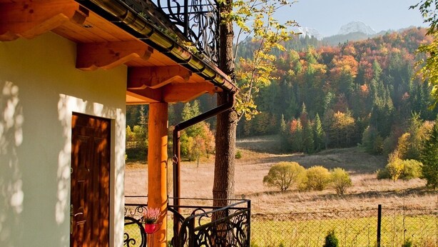 A rustic house with a wooden porch and a metal railing overlooking a scenic valley with trees and mountains. - Willa Bachledowka (Zakopane)