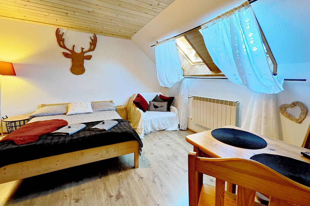 A cozy bedroom with a bed, a wooden table, and a window with curtains.