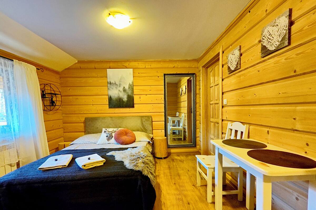 A wooden cabin room with a bed, a small table, and a mirror.