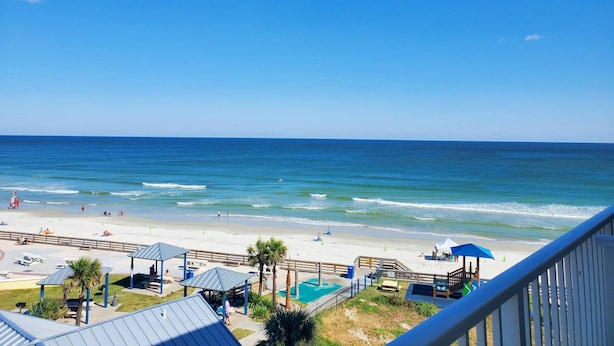 A beach view with a pool area, umbrellas, and beach chairs. - Heated Oceanfront Pool + Hot Tub | Ocean View Studio | Free Daily Activities (Daytona Beach)