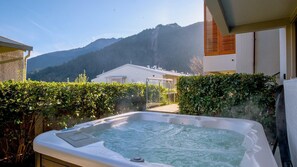 Ett bubbelbad med utsikt över bergen, omgivet av grönska och en modern byggnad.
