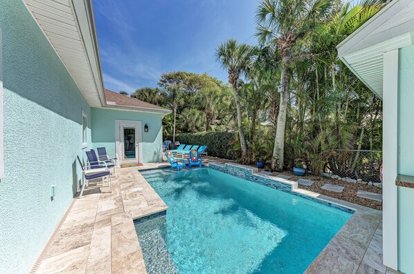A swimming pool with lounge chairs, surrounded by palm trees and a light blue building.