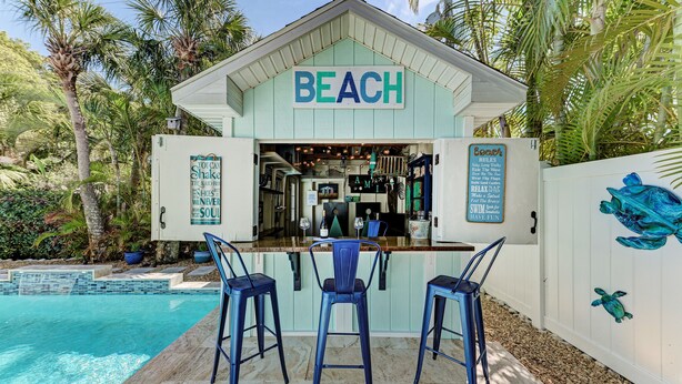Un bar a tema spiaggia con un cartello che recita 'BEACH' e un'area salotto a bordo piscina con tre sedie.