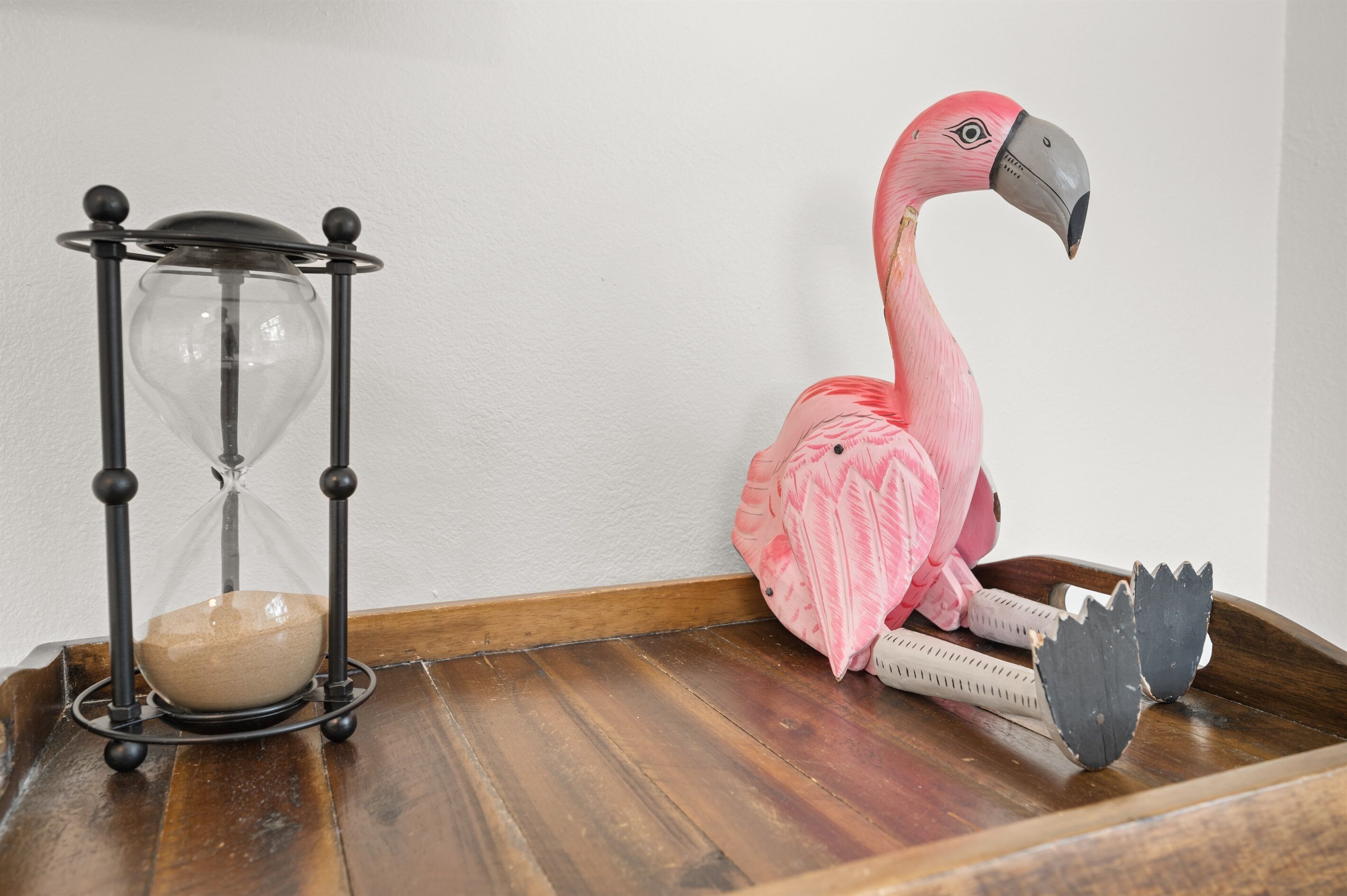 An hourglass and a pink flamingo statue on a wooden tray.