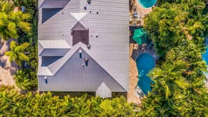 An aerial view of a resort with a pool, surrounded by lush greenery and palm trees.