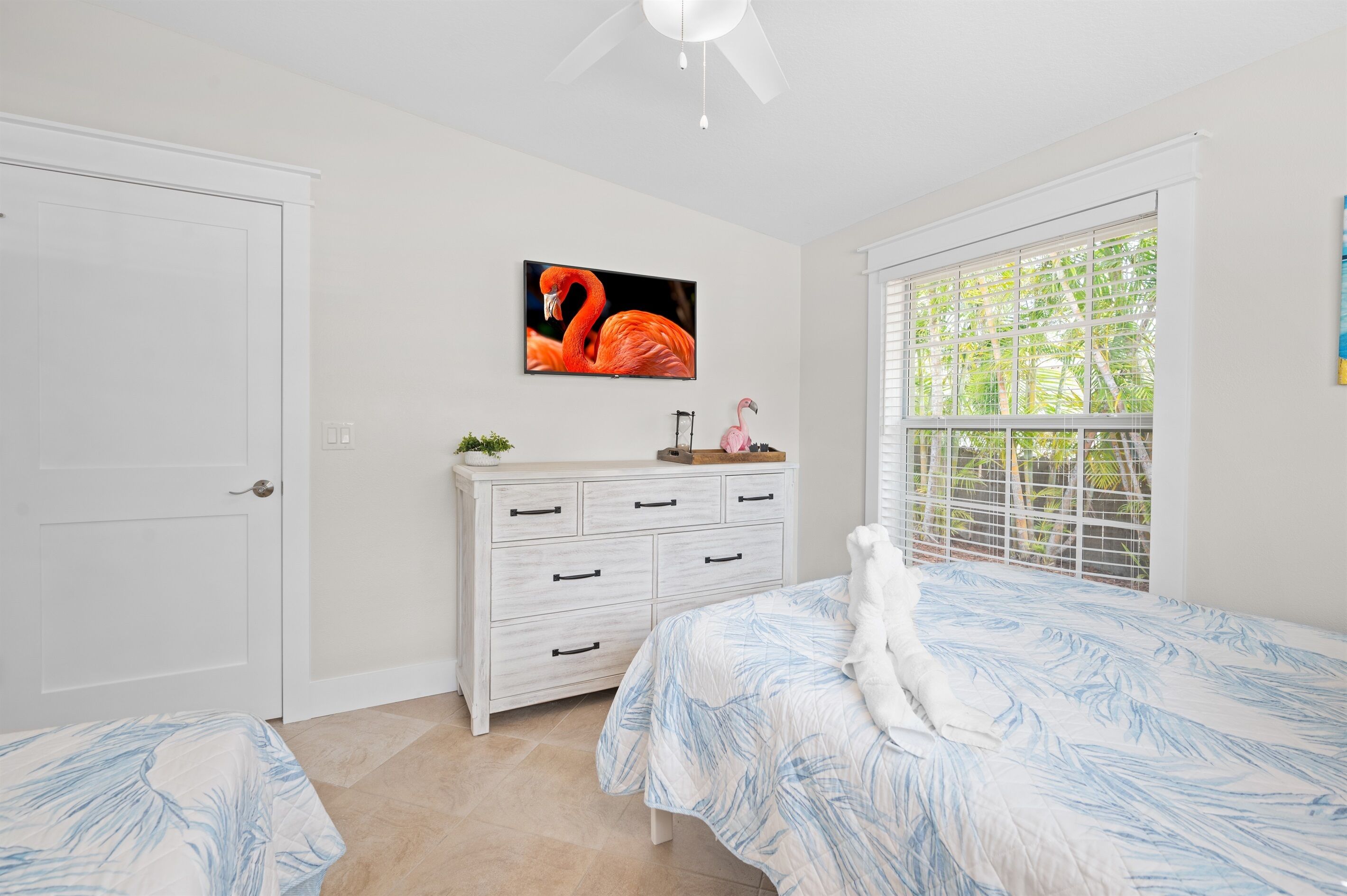 A bedroom with a bed, a dresser, a television, and a window with blinds.
