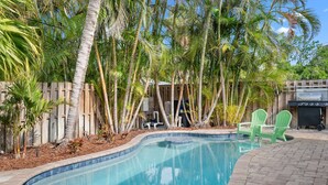 A swimming pool with a wooden deck, surrounded by palm trees and a wooden fence.