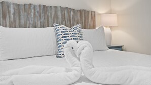 A neatly made bed with white linens and two folded towels on the bed.