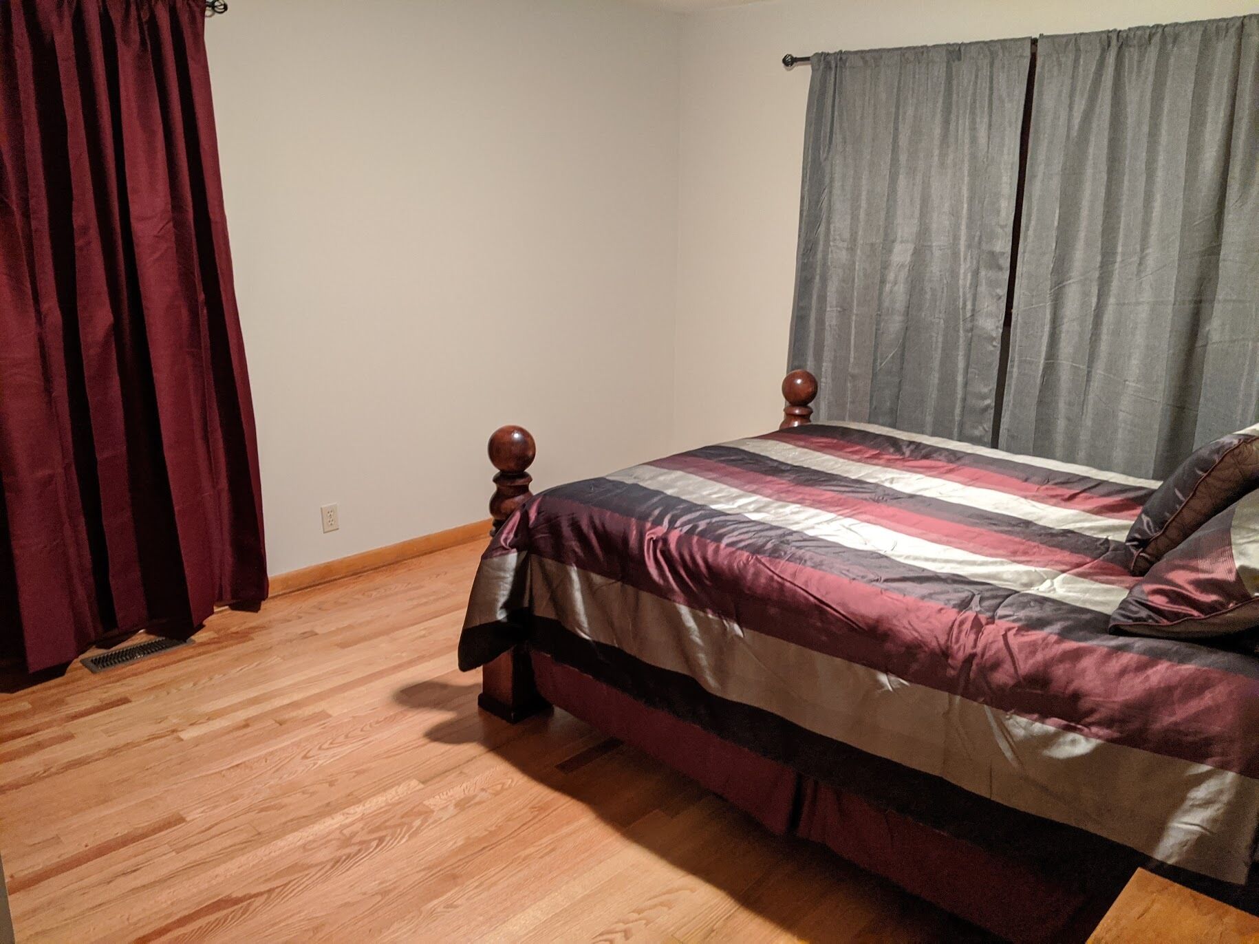 A bedroom with a wooden bed, a dark red curtain, and a grey curtain.