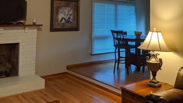 A cozy living room with a fireplace, wooden ceiling beams, a dining area with a table and chairs, and a television on a shelf. - s1. Beautiful home in historic Scottsboro w/ pool (Scottsboro)