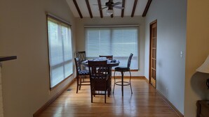 A dining area with a wooden table and chairs, large windows with blinds, and a ceiling fan. - s1. Beautiful home in historic Scottsboro w/ pool (Scottsboro)