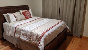 A neatly made bed with a patterned bedspread and pillows, a wooden headboard, and a window with curtains. - s1. Beautiful home in historic Scottsboro w/ pool (Scottsboro)