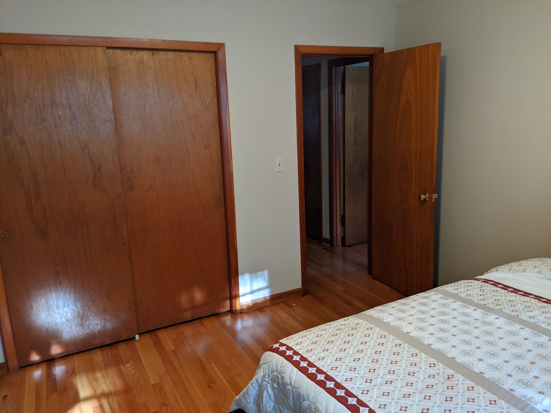 Un dormitorio con piso de madera, una cama con cubrecama estampado y una puerta de madera cerrada.