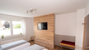 Et moderne hotelværelse med to senge, et fjernsyn ophængt på en træpanel, en lille træskammel og en rød bænk.