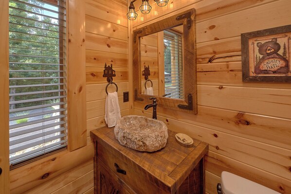 A wooden cabin bathroom with a stone sink, wooden cabinets, a mirror, and a towel rack.