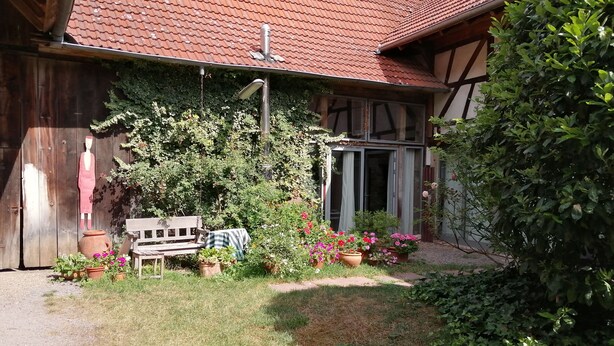 A rustic wooden building with a red-tiled roof, a bench, and potted plants in the yard. - Reizvolles Domizil (Vollmersweiler)