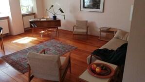 A living room with a wooden floor, a dining table, a sofa, a chair, a small table with fruit, and a painting on the wall. - Reizvolles Domizil (Vollmersweiler)