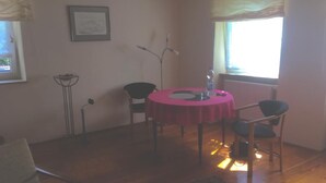 A room with a round table covered by a red tablecloth, two chairs, a floor lamp, a framed picture on the wall, and a window with curtains. - Reizvolles Domizil (Vollmersweiler)