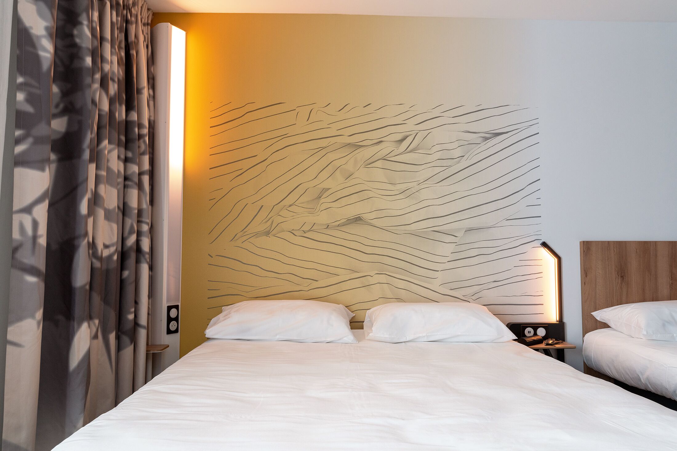 Une chambre d’hôtel dotée d’un grand lit, de deux tables de chevet et d’un mur au revêtement texturé original.