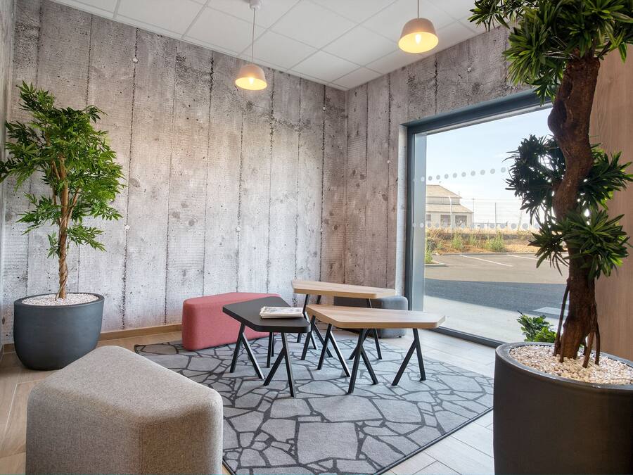 A modern interior with a concrete wall, two potted plants, a red bench, and a table with chairs.