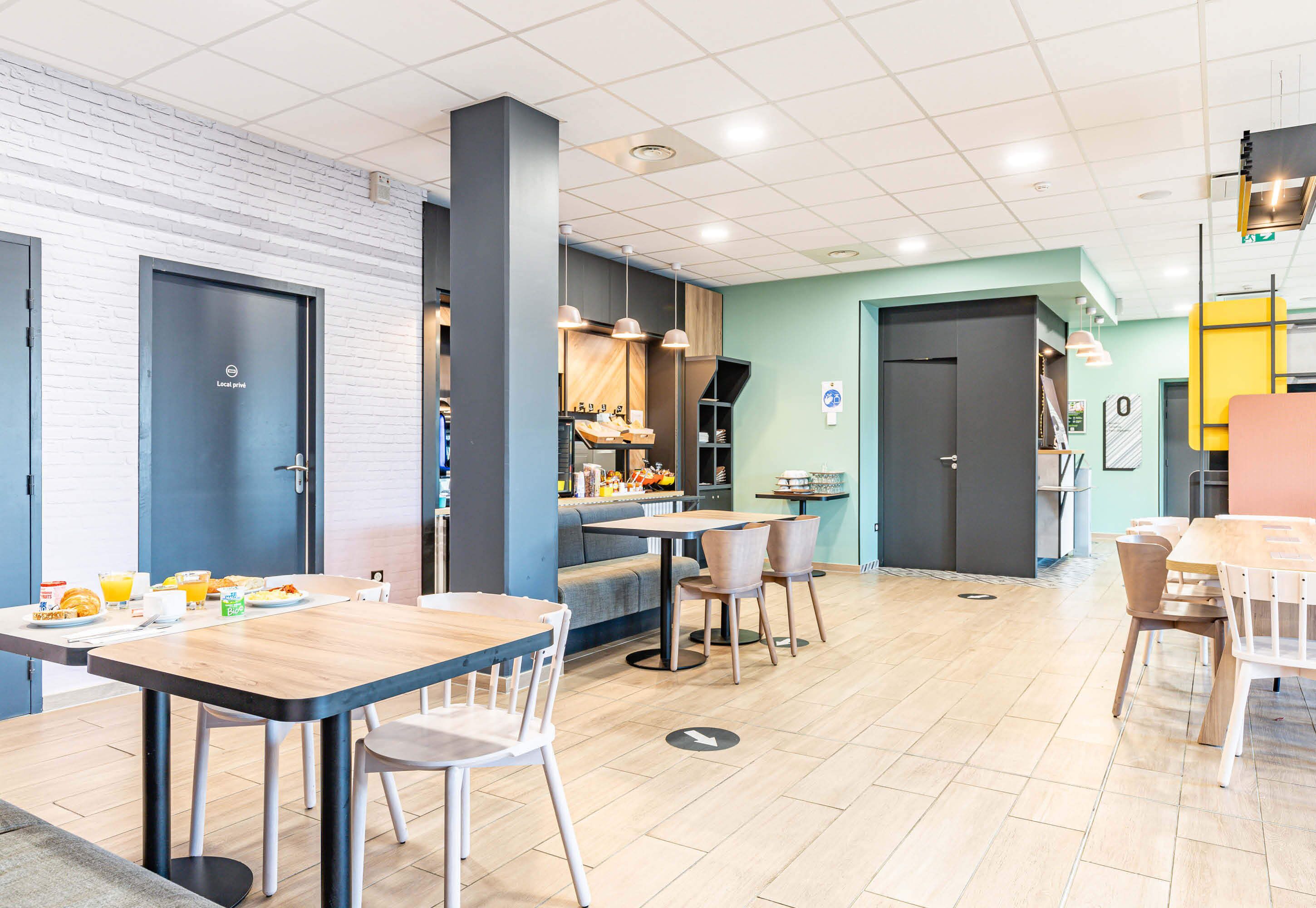 Un comedor moderno con mesas y sillas, una cocina al fondo y una puerta azul con la etiqueta "Lock room".