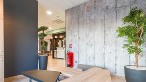 A modern indoor space with a reception area, seating, and a large potted plant. - B&B HOTEL Poitiers Aéroport (Biard)