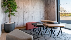 A modern meeting room with a concrete wall, a potted plant, a red bench, and a wooden table with benches. - B&B HOTEL Poitiers Aéroport (Biard)
