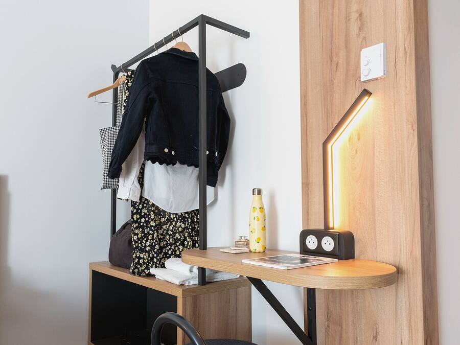 A compact room with a bunk bed, a desk with a lamp, a chair, and a small ottoman.