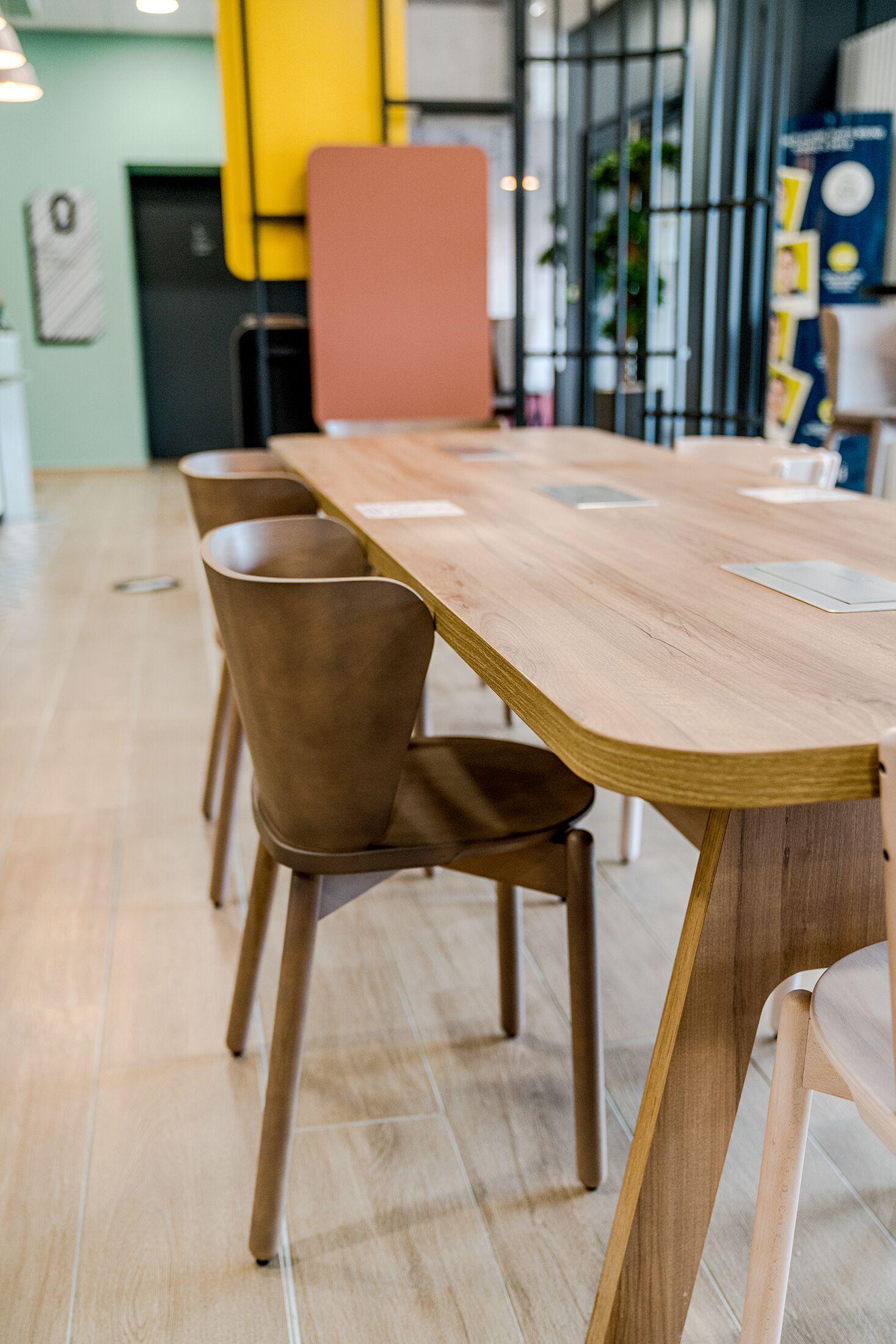 A long wooden table with chairs, a yellow partition, and a black metal gate in a modern interior.