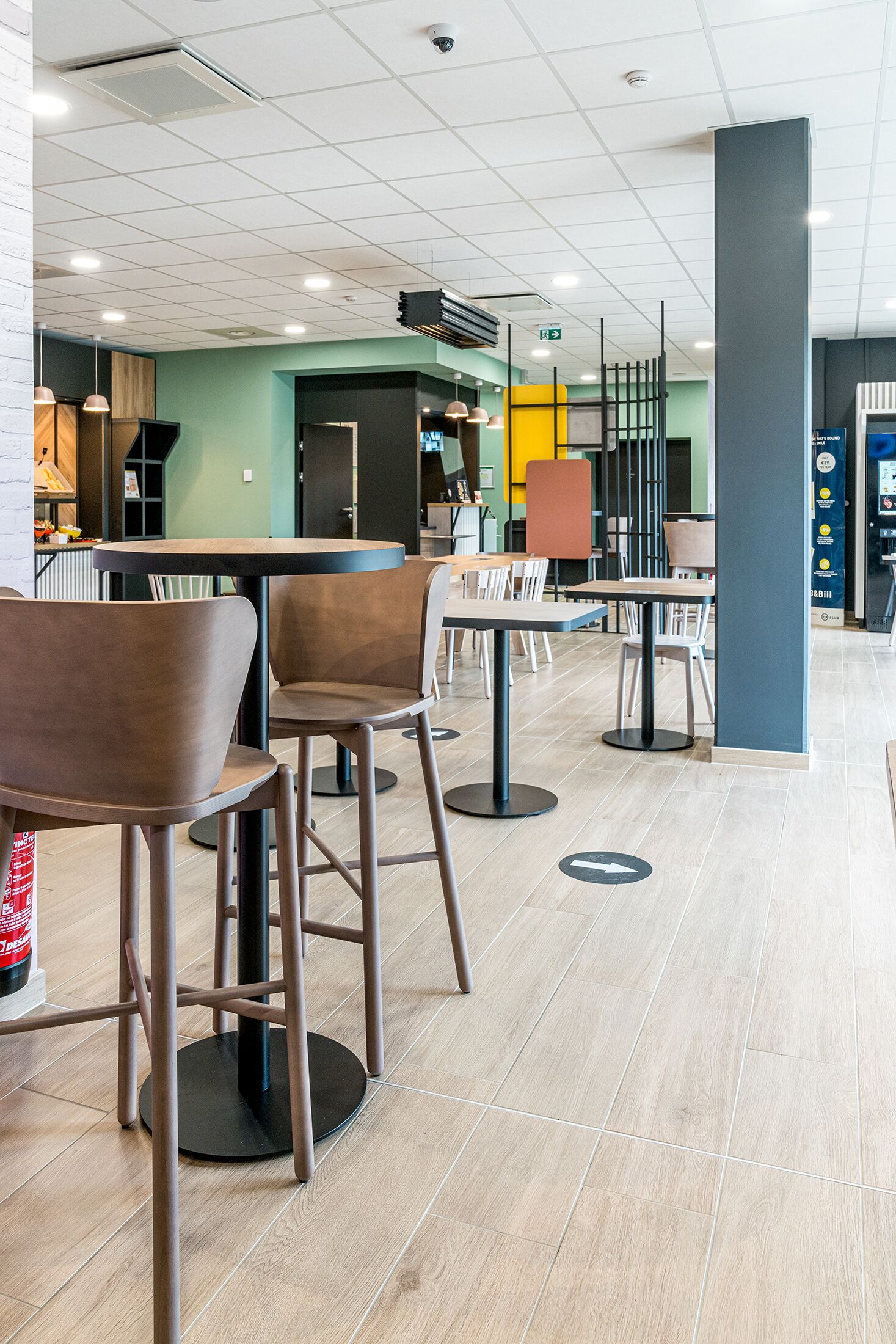 A modern indoor space with multiple seating areas, including round tables and chairs, and a visible fire extinguisher.
