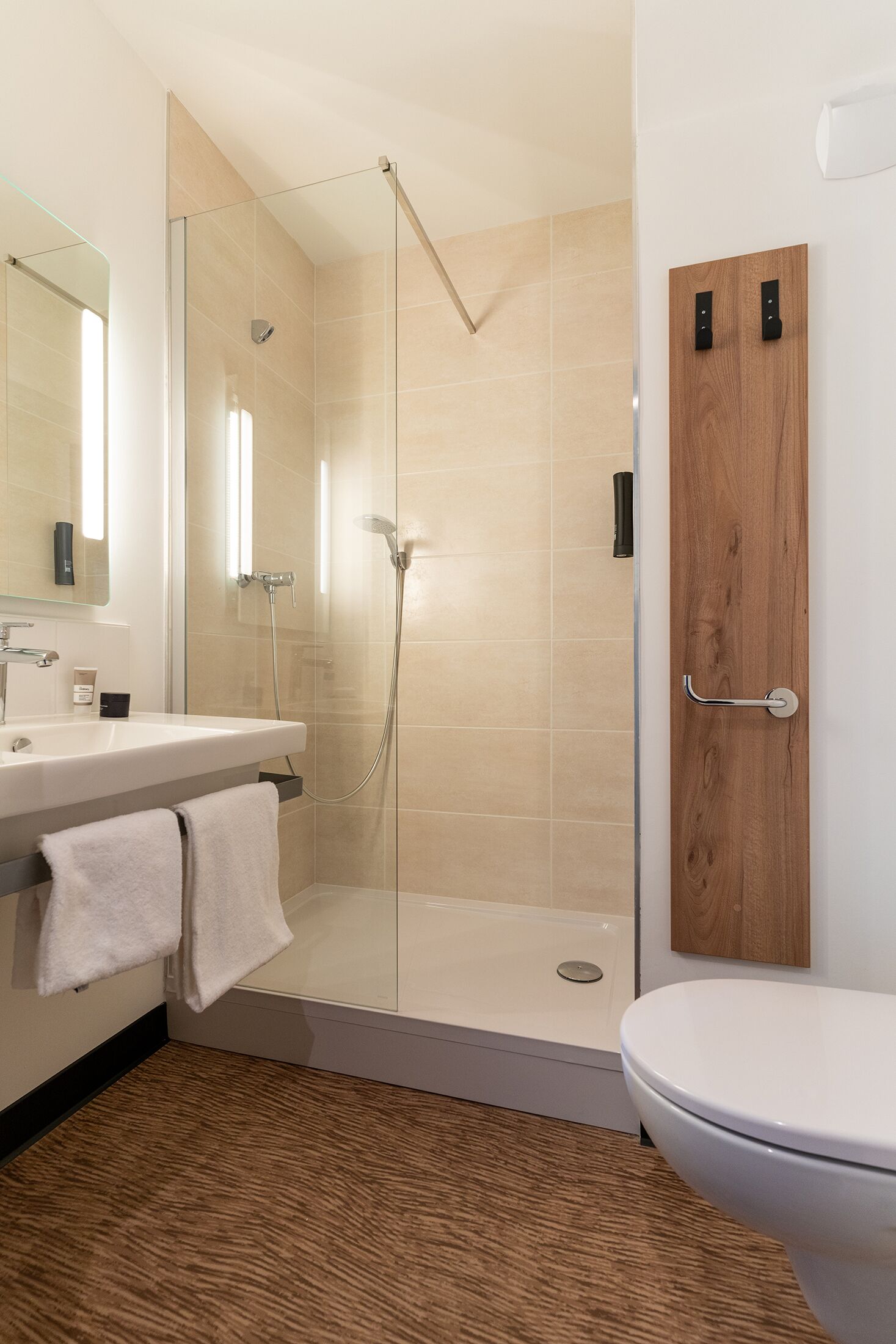 A modern bathroom with a glass-enclosed shower, a wooden door, and a white toilet.