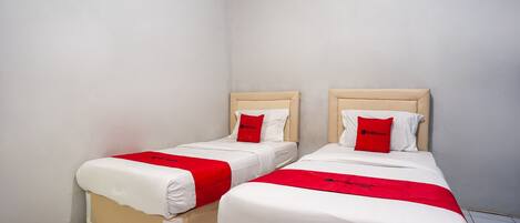 Two single beds with white bedding and red accents, in a corner room with white walls and tiled flooring.