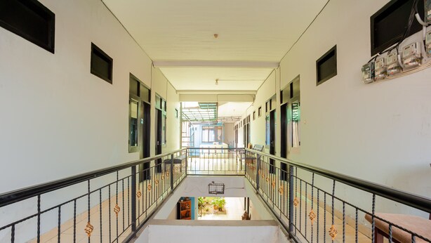 A corridor with a central staircase, metal railings, and a view into a room with a window and a small garden area. - RedDoorz Syariah near Margonda Raya (Depok)