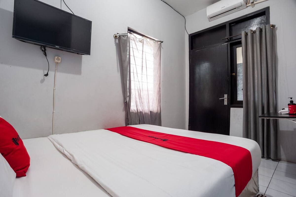 Une chambre d’hôtel avec un lit, un téléviseur fixé au mur, une porte et une fenêtre avec des rideaux.